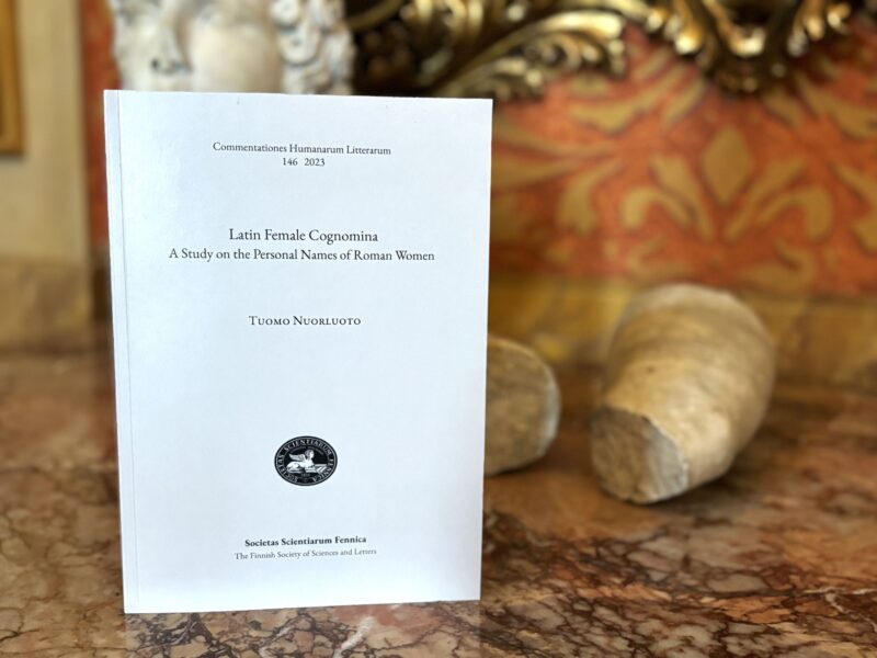 Kuva esiteltävästä kirjasta pöydällä, takana patsaita