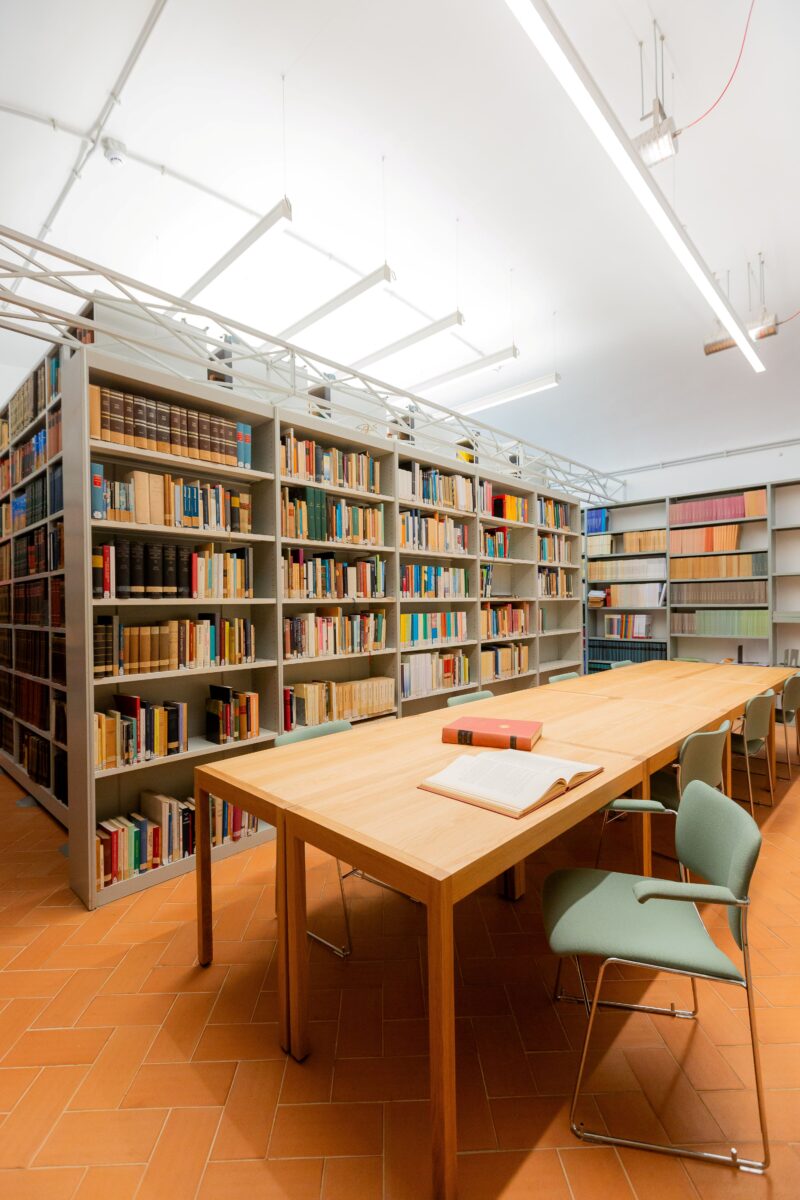 Valokuva instituutin alakirjastosta, josta löytyy puiset pöydät työskentelyyn vaaleanvihreine tuoleineen. Kirjahyllyt näkyvät taustalla.