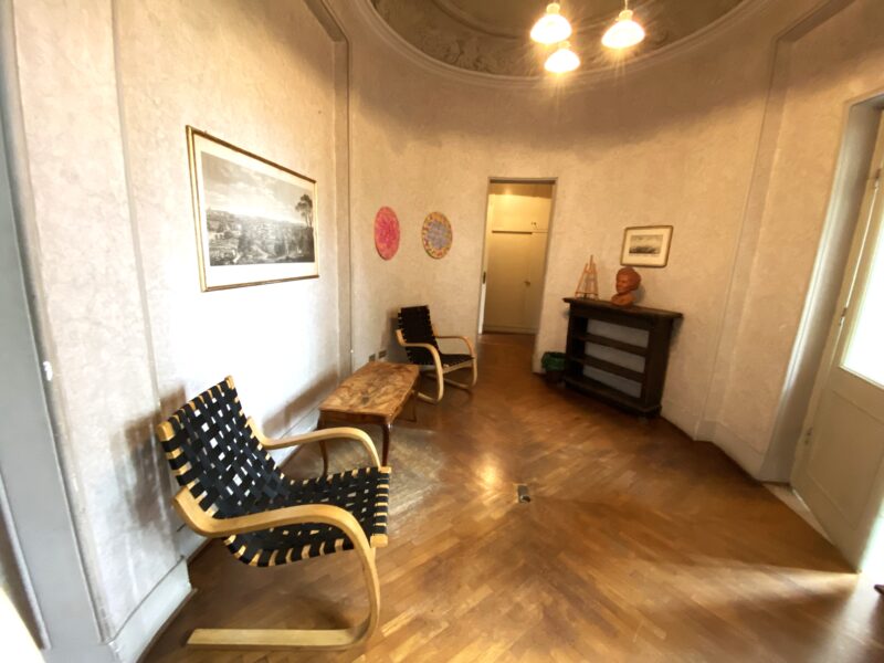 Ovaalinmuotoinen pieni sali, jossa kaksi tuolia ja sohvapöytä.